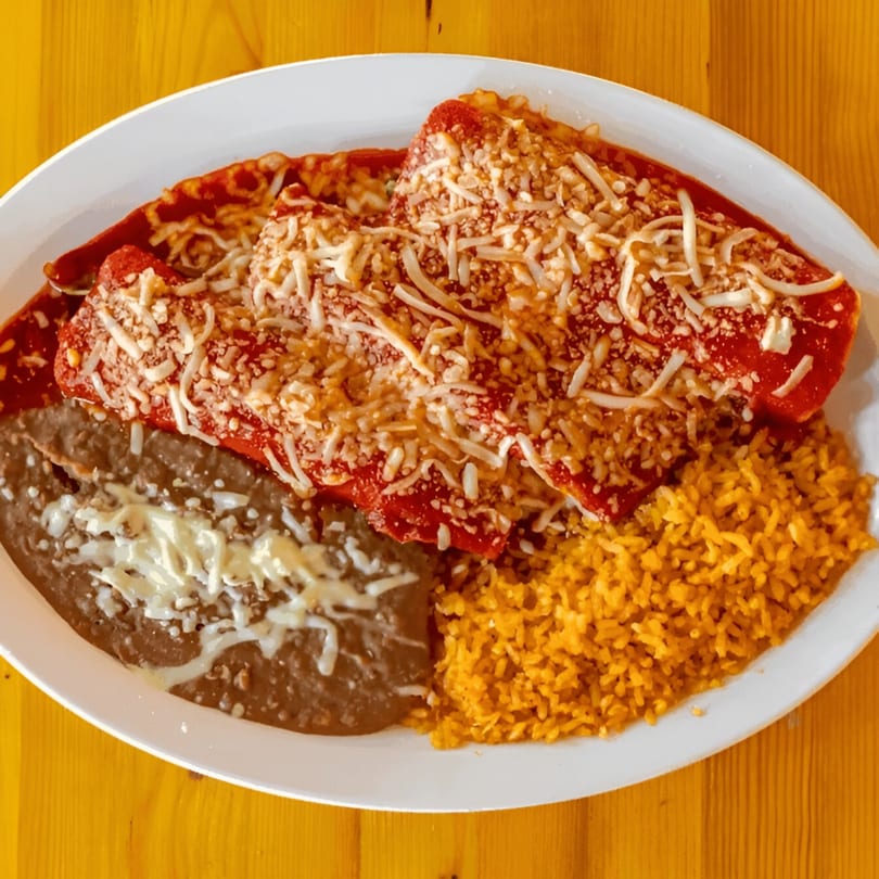 Two cheese enchiladas with red sauce, rice, and refried beans on a white plate.